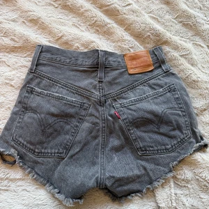 Grå Levi's 501 jeansshorts - Snygga grå jeansshorts från Levi's modell 501 med medelhög midja och råa fransade benslut. Klassisk femficksdesign, knäppning med knappar och perfekta för sommaren!