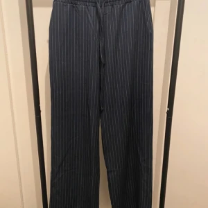 Randiga vida byxor från Amisu - Snygga mörkblå byxor från Amisu med vita tunna ränder. Modellen är wide med resår och snörning i midjan för extra komfort. Byxorna har raka ben och är perfekta för en chill och trendig look. Aldrig använda