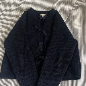 Marin blå stickad långarmadkofta Gina Tricot - Mysig svart stickad cardigan jacka från Gina Tricot med knytband framtill. Jackan har lång ärm och en lite boxig, croppad passform. Perfekt att slänga över en t-shirt för en chill look. Materialet är grovstickat och känns riktigt mjukt.