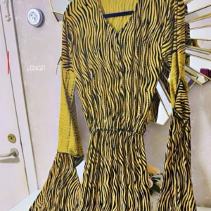 Gul kurdisk klänning - Kurdisk klänning i gult och svart med zebramönster och v-ringning. Klänningen har långa, vida ärmar och resår i midjan för en snygg passform. Perfekt för dig som vill sticka ut och på köpet inkluderas lilla jackan på klänninge. Passar storleken S och M✨