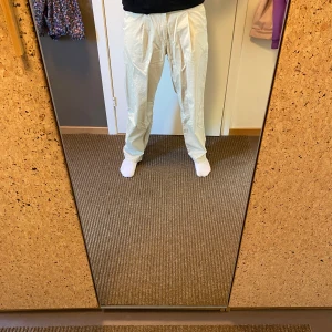 Beiga vida byxor med hög midja - Säljer ett par beiga byxor med hög midja och vida ben. Byxorna har veck framtill och är tillverkade i ett lätt bomullstyg som ger en avslappnad och luftig känsla. Perfekta för dig som gillar en loose och chill stil.