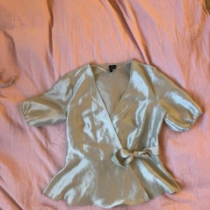 ljus grön omlottblus med knyt - Superfin ljusblå omlottblus i glansigt material med korta puffärmar och knyt i midjan. Blusen har v-ringning och volangkant nedtill som ger en söt och trendig look. Perfekt att styla med jeans eller kjol för en fräsch outfit. Sälja tyvärr då den är för liten💕köpt för 450 och aldrig använd!