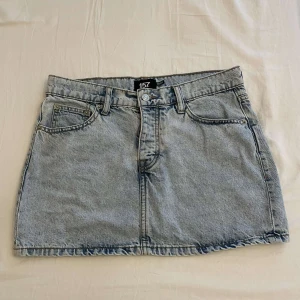 Ljusblå jeanskjol  - Säljer en klassisk ljusblå jeanskjol  med fem fickor, bälteshällor och knapp- samt dragkedjestängning framtill. Perfekt basic-plagg med snygg tvätt och rak passform. Enkel att styla till olika looks!