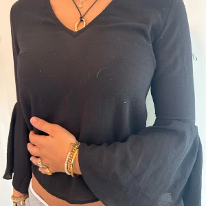 Svart blus med trumpetärmar  - Svart blus med v-ringning, vida trumpetärmar och snygg öppen rygg med knytband. Tunt, lätt material som ger en luftig känsla. Priset är diskuterbart. 