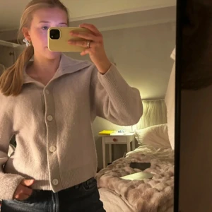 Beige kofta med stora knappar - Supermysig grå kofta med stora knappar och bred krage. Koftan är stickad och har långärmade ärmar samt ribbade muddar. 