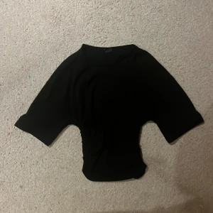 Svart topp från Gina Tricot XS - En svart, enkel topp från Gina Tricot i storlek xs.😄Modellen har korta ärmar och en rund halsringning. Tröjan är skrynklad vid sidorna av midjan. Passar till allt!!💓💓💓😍😍😚