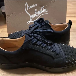 Marinblå sneakers från Christian Louboutin - Snygga marinblå sneakers från Christian Louboutin med coola nitar på tån och klassisk röd sula. Skorna har snörning, rund tå och är tillverkade i skinn och textil. Perfekta för dig som vill sticka ut med en edgy vibe.