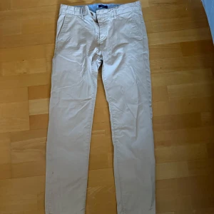 Beige chinos från Gant, 158/164cm - Snygga beige chinos från Gant i klassisk rak modell. Byxorna har sidfickor, bälteshällor och är tillverkade i mjuk bomull. Perfekta för en clean och stilren look, passar både till skjorta och t-shirt.