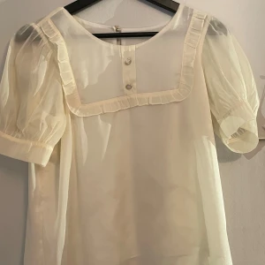 Ljusvit o gulaktig blus med volang och puffärm - Helt ny, oanvänd svart blus, står ingen storlek i tröjan men skulle säga storlek S! Står inte heller vilket märke!