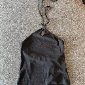 Svart halterneck linne med knyt - Säljer ett svart halterneck linne med smala knytband i nacken och en liten cut-out framtill. Toppen är ärmlös 🩷
