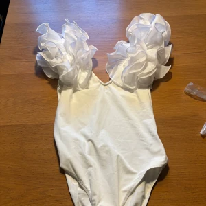 Vit topp med volangärmar - Superfin vit topp med stora, fluffiga volangärmar som verkligen sticker ut. Djup v-ringning fram och knäppning i grenen för extra smidighet. Materialet är stretchigt och känns bekvämt mot huden. Perfekt för dig som vill ha något unikt.