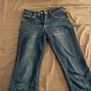 Blå jeans med kontrastsömmar - Snygga blå jeans med markerade vita kontrastsömmar och unika bakfickor med dekorativa detaljer och knappar. Klassisk femficksmodell med dragkedja och knapp framtill. Jeansen har en rak passform och är tillverkade i denim.