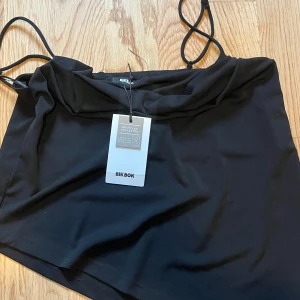 Svart asymmetrisk linnetopp Bik Bok - Svart linnetopp från Bik Bok med smala axelband och cool asymmetrisk nederkant. Tillverkad i återvunnen polyester som känns lätt och smidig. Perfekt för dig som gillar minimalistisk stil med en twist.