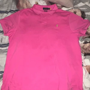 Rosa pikétröja Polo Ralph Lauren XL - Säljer en rosa pikétröja från Polo Ralph Lauren i modellen Custom Slim Fit. Tröjan har klassisk krage, knäppning med två knappar och den ikoniska gröna loggan broderad på bröstet. Tillverkad i bomull och passar perfekt för en fräsch och sportig look. Priset kan diskuteras 
