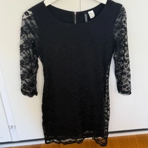 Svart spetsklänning från H&M Divided - Supersnygg svart kortklänning från H&M Divided med spetsdetaljer och trekvartsärm. Klänningen har figurnära passform, dragkedja i ryggen och transparenta ärmar i spets. Perfekt för dig som vill sticka ut med en klassisk look.