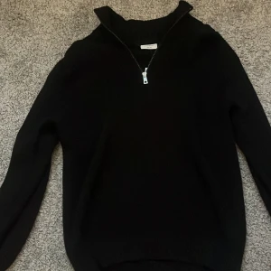 Svart stickad half zip-tröja Kappahl - Svart stickad tröja från Kappahl med half zip-dragkedja i halsen. Tröjan har lång ärm och ribbade muddar vid hals, ärmslut och nederkant. Perfekt för lager-på-lager och chill stil under kyliga dagar.