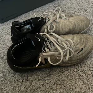 Nike fotbollsskor i svart och grått Elite  - Snygga fotbollsskor från Nike med stickad ovandel i grått och svart, vita skosnören och svarta detaljer. Skorna har en låg profil och slitstark sula med dobbar för bra grepp på planen. Perfekta för dig som vill ha stil och funktion på fotbollsplanen.