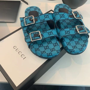 Blå sandaler från Gucci med monogram - Snygga blå sandaler från Gucci med dubbla spännen i silver och klassiskt GG-monogram över hela skon. Tillverkade i textil med svarta detaljer och robust sula. Perfekta för dig som vill sticka ut med en lyxig och trendig look. Kvitto finns