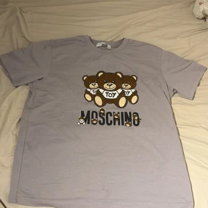 Ljuslila Moschino t-shirt med björnar - Säljer en ljuslila t-shirt från Love Moschino i bomull med tryck av tre söta björnar och stor logga på bröstet. Klassisk passform och korta ärmar, perfekt för dig som gillar statement-plagg och lekfull stil. Är ett XL men sitter som ett L