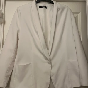 Vit kavaj från Gina Tricot, stl 36 - Snygg vit kavaj från Gina Tricot i storlek 36. Kavajen har en klassisk passform med en knapp framtill, två fickor och mjukt foder. Perfekt för dig som vill ha en stilren och fräsch look. Enkel att matcha med både jeans och kjol.