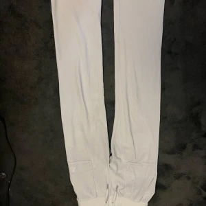 Vita mjukisbyxor från juicy couture med snörning - Snygga vita mjukisbyxor från juicy couture  med broderad logga på benet, snörning i midjan och praktiska fickor med lock och knappar bak. Mjukt material och ribbade muddar vid benslut. Perfekta för chill eller streetwear. Höger backficka har en söm som har låsnat.