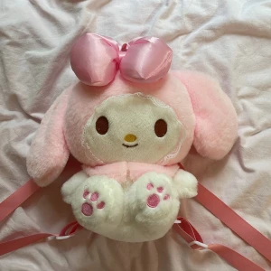 My Melody ryggsäck i plysch - Supergullig My Melody ryggsäck i mjuk plysch med stora rosa öron, söt rosett och broderade tassar. Väskan har dragkedja och justerbara band i rosa. Perfekt för dig som älskar kawaii och vill sticka ut med en unik accessoar! Aldrig använd och mycket bra skick.