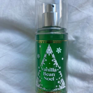 Vanilla Bean Noel mist Bath & Body Works - En grön parfymmist från Bath & Body Works med doften Vanilla Bean Noel. Flaskan har ett vintrigt design med vita snöflingor och en julgran, samt en silvrig spraytopp och genomskinligt lock. Perfekt för dig som älskar söta, vaniljiga dofter.