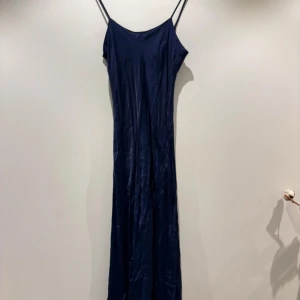 Marinblå långklänning från Zara XS - Säljer en stilren marinblå långklänning från Zara i slinky satinliknande material. Klänningen har tunna axelband och en rak, elegant siluett som faller snyggt längs kroppen. Perfekt för dig som gillar minimalistisk och trendig stil.