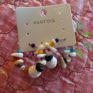 Färgglada örhängen från Parfois - Unika örhängen från Parfois med pärlor i olika former och färger som vitt, lila, turkos, orange och svart. Designen är lekfull med inslag av snäckor och pärlliknande detaljer, perfekt för dig som vill sticka ut med accessoarer.