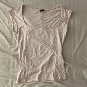 Ljusrosa linnetopp från Gina Tricot - Supersöt ljusrosa linnetopp från Gina Tricot med fyrkantig ringning och ärmlös design. Perfekt att styla med jeans eller kjol för en fräsch look. Tunt och mjukt material som känns skönt mot huden.