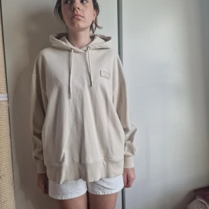 Beige hoodie från Calvin Klein - Säljer en oversized beige hoodie från Calvin Klein med broderad CK-logga på bröstet. Tröjan har huva med snörning, långa ärmar och ribbade muddar. Perfekt för en chill och avslappnad stil.