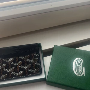 Goyard plånbok/ korthållare  - Säljer en stilren plånbok från Goyard med deras klassiska grafiska mönster i svart, brunt och vitt. Plånboken är i skinn och har flera kortfack, perfekt för dig som vill ha något både snyggt och praktiskt i fickan.