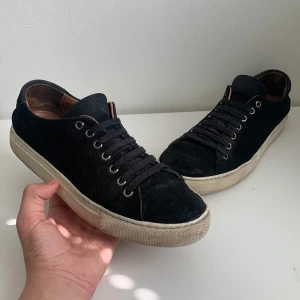 Svarta mockasneakers från Human Scales - Stilrena svarta sneakers i mocka från Human Scales med klassisk vit sula och svarta snören. Insidan är fodrad med brunt skinn för extra komfort. Perfekta för dig som gillar en clean och tidlös look. Rund tå och platt sula ger en avslappnad vibe. Nypris 1999,vårt pris 400!