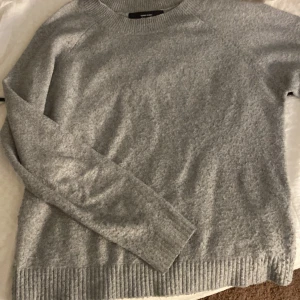 Grå stickad tröja från Vero Moda - Mysig grå stickad tröja från Vero Moda i storlek M. Tröjan har en klassisk rund halsringning, långa ärmar och ribbade muddar vid ärmslut och nederkant. Perfekt för lager-på-lager och chill dagar.
