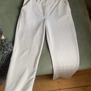Beiga raka kostymbyxor - Snygga vita kostymbyxor med raka ben och klassisk passform. Byxorna har fickor i sidorna, bälteshällor och stängs med knapp och dragkedja. Perfekta för en clean och stilren look.