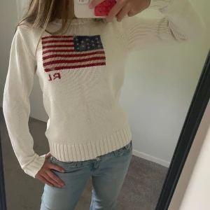 Vit stickad tröja Polo Ralph Lauren - Vit stickad tröja från Polo Ralph Lauren med amerikansk flagga broderad på bröstet. Tröjan har rund hals, ribbade muddar och är långärmad. Aldrig använd. Pris kan diskuteras vid snabb köp.