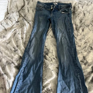 Blå bootcut jeans från Gina Tricot - Snygga blå jeans från Gina Tricot i bootcut-modell med klassisk femficksdesign och dubbla silverknappar i midjan. Jeansen har en lätt tvättad look och är tillverkade i mjukt denimtyg som sitter skönt hela dagen.