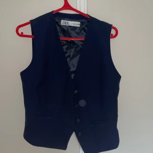 Mörkblå väst från Zara med knappar - Stilren mörkblå väst från Zara med klassisk v-ringning och knäppning framtill. västen är fodrad med slätt tyg på insidan. Den är knappt använd.