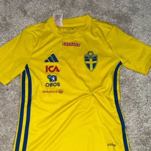 Svenska landslagets fotbollströja Adidas - Gul fotbollströja från Adidas med flera sponsorer och svenska landslagets emblem på bröstet. Tillverkad i lätt och ventilerande material, perfekt för träning eller match.
