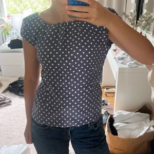 Prickig blus från Newhouse - Supersöt mörkblå blus från Newhouse med vita prickar. Blusen har korta ärmar och rund halsringning, perfekt för en fräsch och lekfull look. Tillverkad i ett lätt och luftigt bomullstyg som känns skönt mot huden.