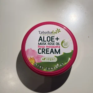 Tabaiabaloe Aloe+ Musk Rose Cream - Vegansk ansiktskräm med aloe vera och muskrosolja från Tabaiabaloe. Kommer i en rund burk med rosa lock och vit etikett. Innehåller 100% kanarisk aloe vera och är märkt som veganvänlig. Perfekt för återfuktning och mjuk hud.