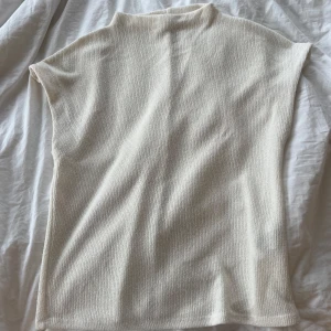 Beige ribbad polotopp - Säljer en stilren beige polotopp med ribbad struktur. Toppen är ärmlös och har en hög hals, vilket ger en clean och modern look. Perfekt att styla med jeans eller kjol för en enkel men snygg outfit.
