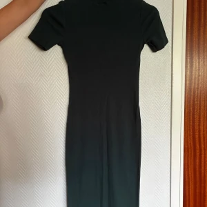 Mörkgrön ribbad klänning från Zara - Snygg mörkgrön ribbad klänning från Zara med korta ärmar och kroppsnära passform. Klänningen har en enkel, stilren design och är tillverkad i ett stretchigt material som sitter skönt. .