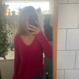 Rosa kabelstickad tröja Ralph Lauren - Säljer en kabelstickad rosa tröja från Ralph Lauren Sport i 100% bomull. Tröjan har v-ringning, lång ärm och klassisk blå broderad logga på bröstet. Perfekt till jeans för en chill och snygg look.