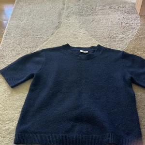 Mörkblå stickad tröja - Mörkblå stickad tröja från Kappahl i storlek 158/164. Tröjan har korta ärmar, rund halsringning och ribbade muddar vid ärmslut och nederkant. Tröjan har ett skönt materiall. 
