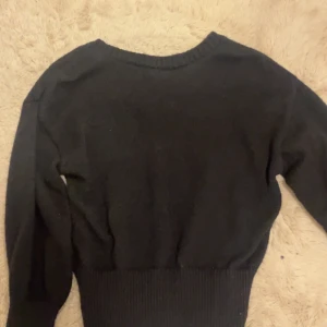 Svart stickad tröja med öppet rygg  - Svart stickad tröja med öppet rygg som har en knytning på baksidan. Tröjan har långa ärmar och bred ribbad mudd i midjan som ger en schysst passform. Perfekt för dig som gillar en enkel men ändå trendig look.