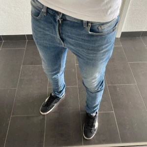 Tiger Of Sweden Jeans - Säljer ett par snygga blå jeans från Tiger Of Sweden , modell LEON. Jeansen har en slim passform med klassisk femficksdesign och ljusa slitningar framtill. Tillverkade i bomull och perfekta för dig som gillar en modern och stilren look.