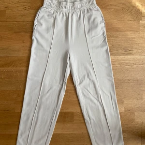 Beiga byxor med resår från H&M - Snygga beiga byxor från H&M med bred resår i midjan och raka ben. Byxorna har fickor i sidorna och är gjorda i ett mjukt material.