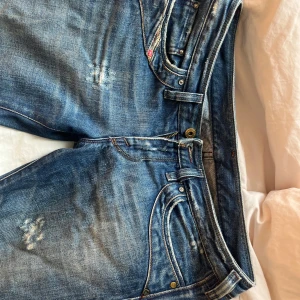 bootcut jeans diesel - Säljer ett par blå bootcut jeans från Diesel med slitna detaljer och klassiska bakfickor. Jeansen har låg midja och är i storlek 28