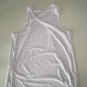Vit ribbad linnetopp - Säljer en vit ribbad linnetopp med klassisk racerback-skärning. Toppen är ärmlös och har en tight passform som sitter snyggt mot kroppen. Perfekt för varma dagar eller som lager under andra plagg.